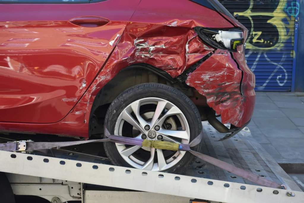 A damaged red car being towed after being crashed into