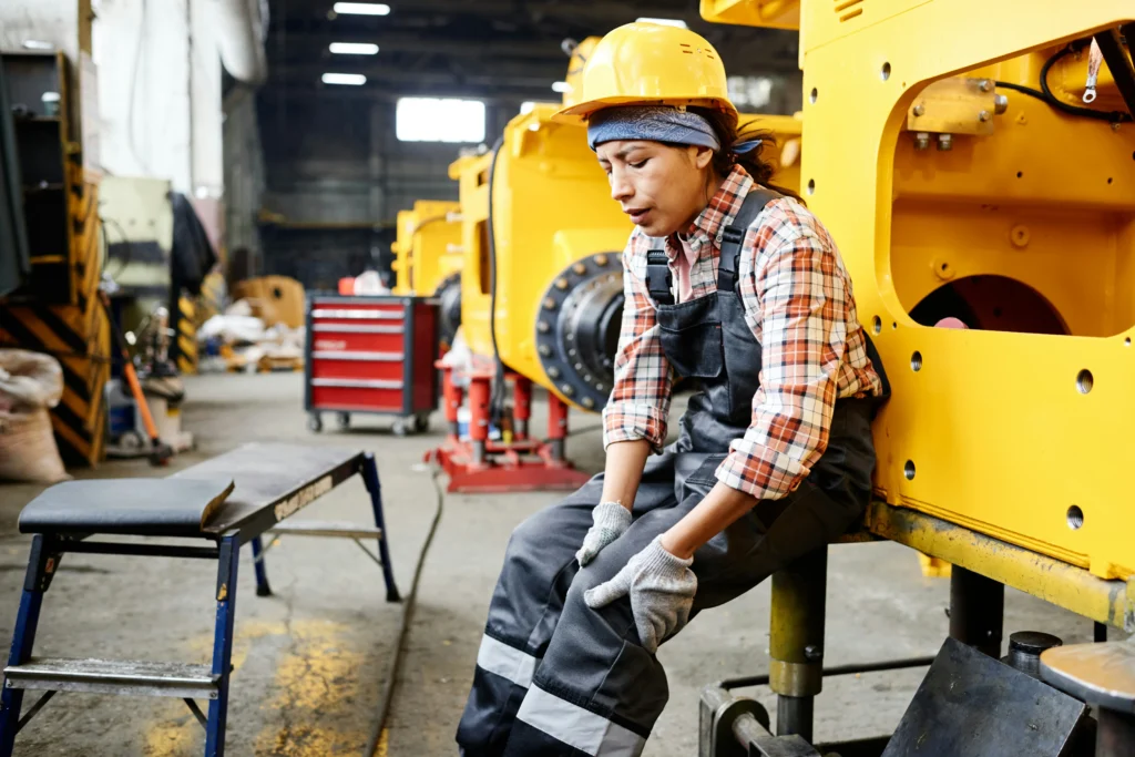 Factory worker in hard hat holding knee after workplace injury